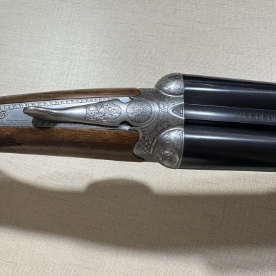 Espingarda com coronha de madeira e metal gravado, canos pretos com texto Beretta.