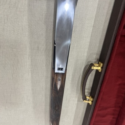 Espingarda com coronha em madeira escura e cano metálico polido ao lado de mala rígida vermelha