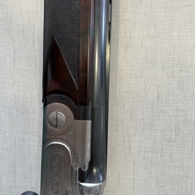 Espingarda de canos paralelos com empunhadura de madeira e acabamento metálico gravado