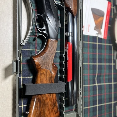 Espingarda de caça com coronha em madeira castanha e cano preto numa mala forrada a tecido xadrez