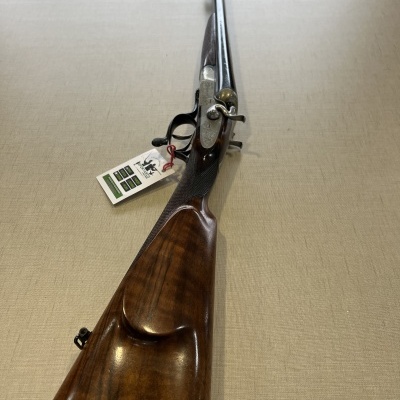 Espingarda de dois canos com coronha em madeira polida sobre superfície bege