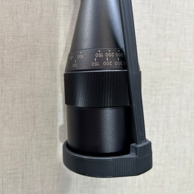 Lente óptica preta com anéis de ajuste numerados montada em suporte preto sobre fundo cinza claro