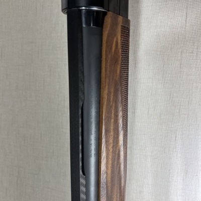 Arma com coronha em madeira e cano metálico preto sobre fundo cinzento