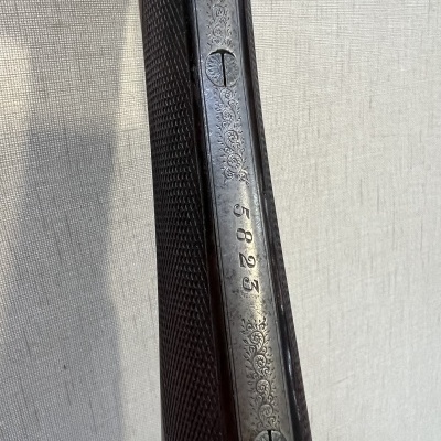 Detalhe de arma de caça com cabo de madeira e parte metálica com número 5823