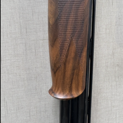 Coronha de espingarda em madeira castanha com textura quadriculada e canos metálicos pretos