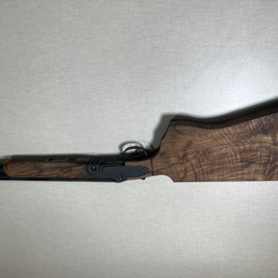 Espingarda de caça com coronha de madeira escura e cano preto encostada numa parede clara