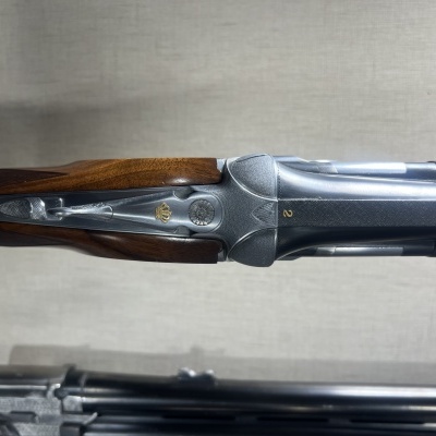 Arma de caça com coronha em madeira e corpo metálico sobre fundo claro