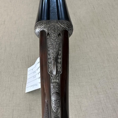 Espingarda de canos duplos com detalhes em metal gravado sobre fundo bege