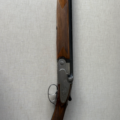 Espingarda de caça com parte em madeira e metal encostada em parede cinzenta