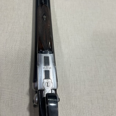 Espingarda de canos duplos com empunhadura em madeira e detalhes metálicos sobre tecido bege