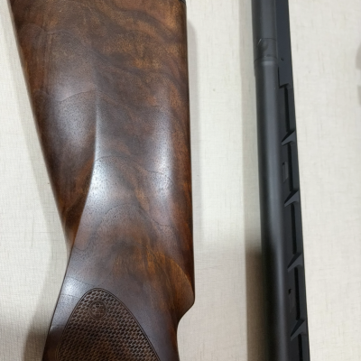 Parte traseira em madeira escura e cano metálico preto fosco sobre tecido claro.