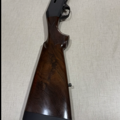 Espingarda com coronha em madeira escura e parte de metal preta sobre superfície clara