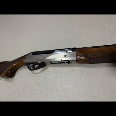 Espingarda Benelli de madeira castanha e metal prateado sobre superfície bege.