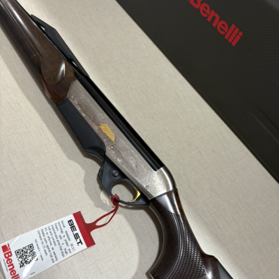 Espingarda Benelli de metal prateado com detalhes gravados e empunhadura de madeira escura colocada sobre superfície clara