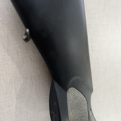 Espigão de arma preta com detalhes de textura cinza, fundo neutro.