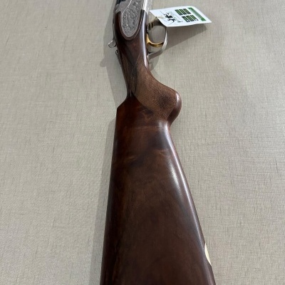 Vista lateral de arma de caça com coronha em madeira castanha escura e detalhes metálicos