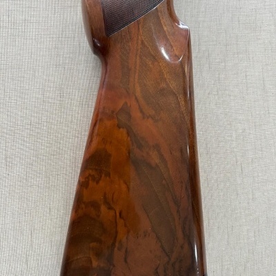 Cabo traseiro de arma de fogo em madeira polida castanha com detalhes texturizados.