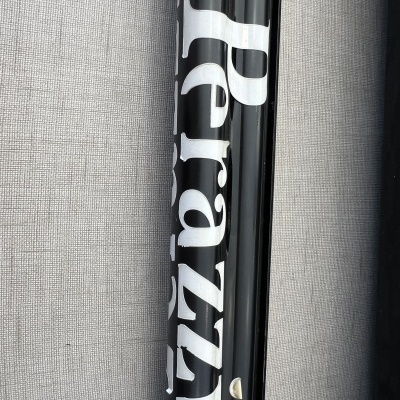 Tubo preto brilhante com texto branco 'Pirazzi' sobre tecido cinzento