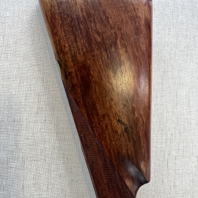 Coronha de espingarda em madeira castanha com textura polida e detalhe em relevo