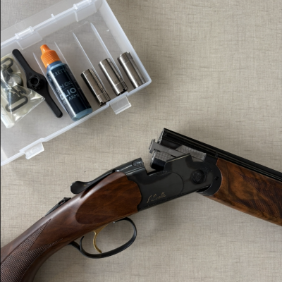 Espingarda de canos duplos aberta com acessórios numa caixa plástica