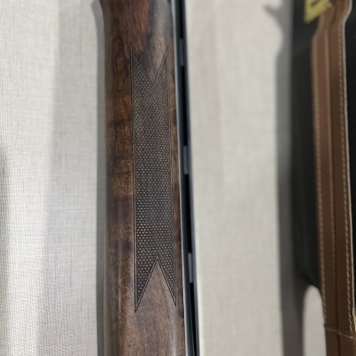 Corpo de espingarda com punho de madeira castanha texturizada e mala preta ao lado