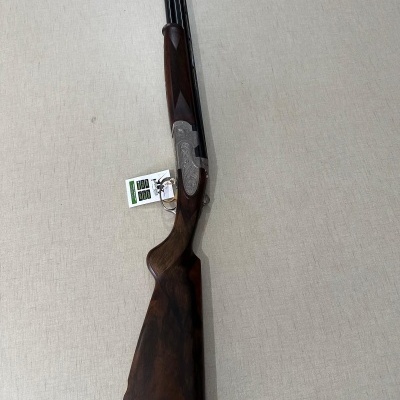 Espingarda com coronha em madeira escura e canos pretos sobre tecido cinza claro