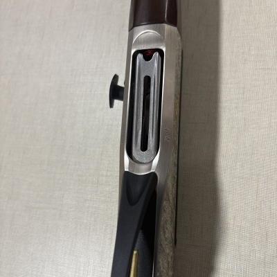 Espingarda com coronha em madeira escura, corpo metálico gravado e carregador aberto com munição visível