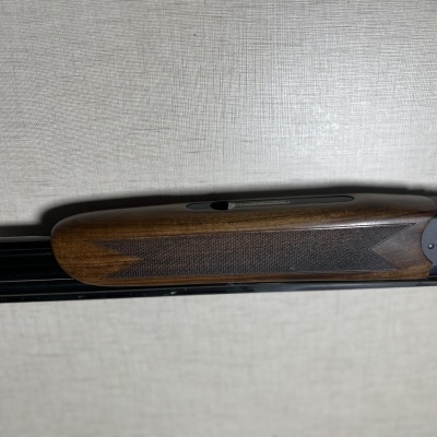 Espingarda com madeira castanha e cano preto sobre superfície clara