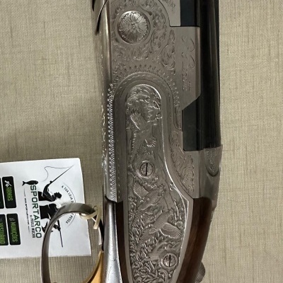 Espingarda com detalhes metálicos, gatilho dourado, empunhadura de madeira e etiqueta branca com texto SPORTARCO