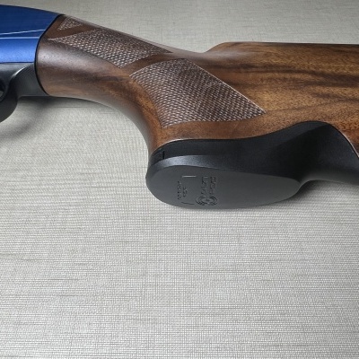 Parte traseira de arma de fogo com coronha em madeira castanha e extremidade preta com inscrições