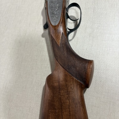 Espingarda com coronha de madeira castanha e mecanismo metálico prateado gravado.