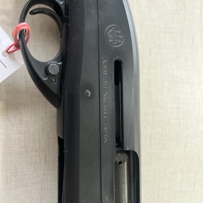 Espingarda preta com gatilho e marcações visíveis num fundo de tecido claro