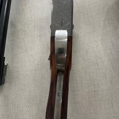 Espingarda com coronha de madeira e parte superior metálica decorada sobre tecido bege