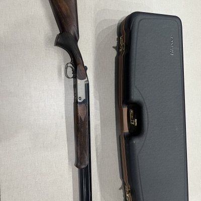 Espingarda com coronha e punho de madeira negra ao lado de estojo rígido preto com fechos dourados