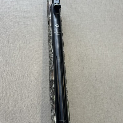 Espingarda de cano longo com acabamento preto e padrão de camuflagem no cabo sobre superfície bege