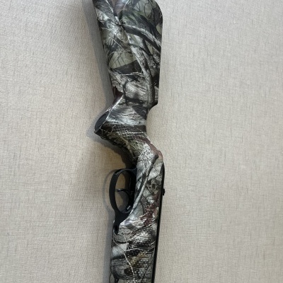 Espingarda camuflada com gatilho preto em superfície clara