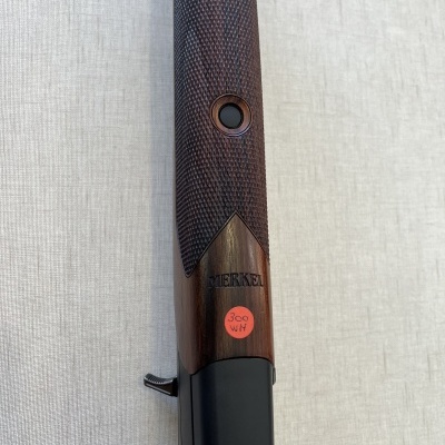 Punho de arma de fogo em madeira castanha com textura xadrez e marca MERKEL