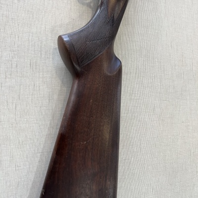 Coronha de rifle em madeira escura com detalhes em relevo e metal, sobre tecido claro