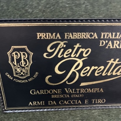 Etiqueta preta com texto dourado da Pietro Beretta numa superfície verde