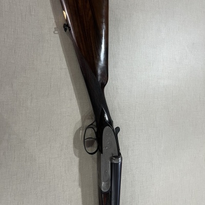 Espingarda dupla com coronha de madeira escura encostada numa parede clara