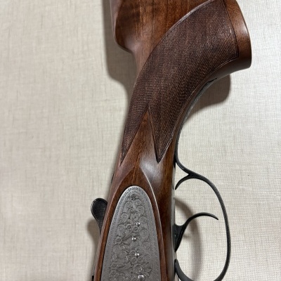 Parte da coronha e gatilho de uma espingarda com detalhes gravados em metal e madeira castanha texturada