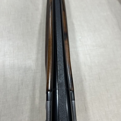 Arma de cano duplo com madeiras marrons e metal preto vista de cima sobre tecido branco