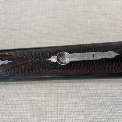 Placa lateral de espingarda com madeira escura trabalhada e detalhes metálicos prateados