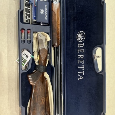 Estojo azul com espingarda Beretta desmontada em madeira e metal, cartuchos e manual