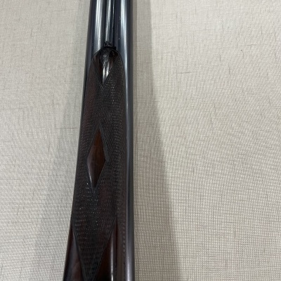 Parte de arma de cano duplo com madeira trabalhada e metal brilhante em tecido claro