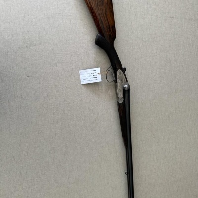 Espingarda com coronha em madeira e canos metálicos sobreposta à parede clara