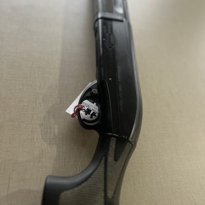 Espingarda preta com empunhadura texturizada e etiqueta no mecanismo de disparo