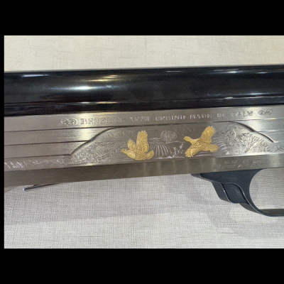 Parte lateral de arma com gravados de patos dourados e texto Benelli-Armi Urbino Made in Italy