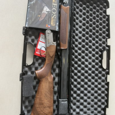 Estojo aberto com espingarda de canos duplos em madeira e metal, manual e acessórios.