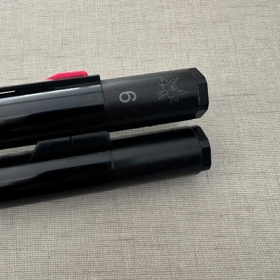 Duas canetas pretas sobre superfície bege com número 6 e símbolo gravado na tampa